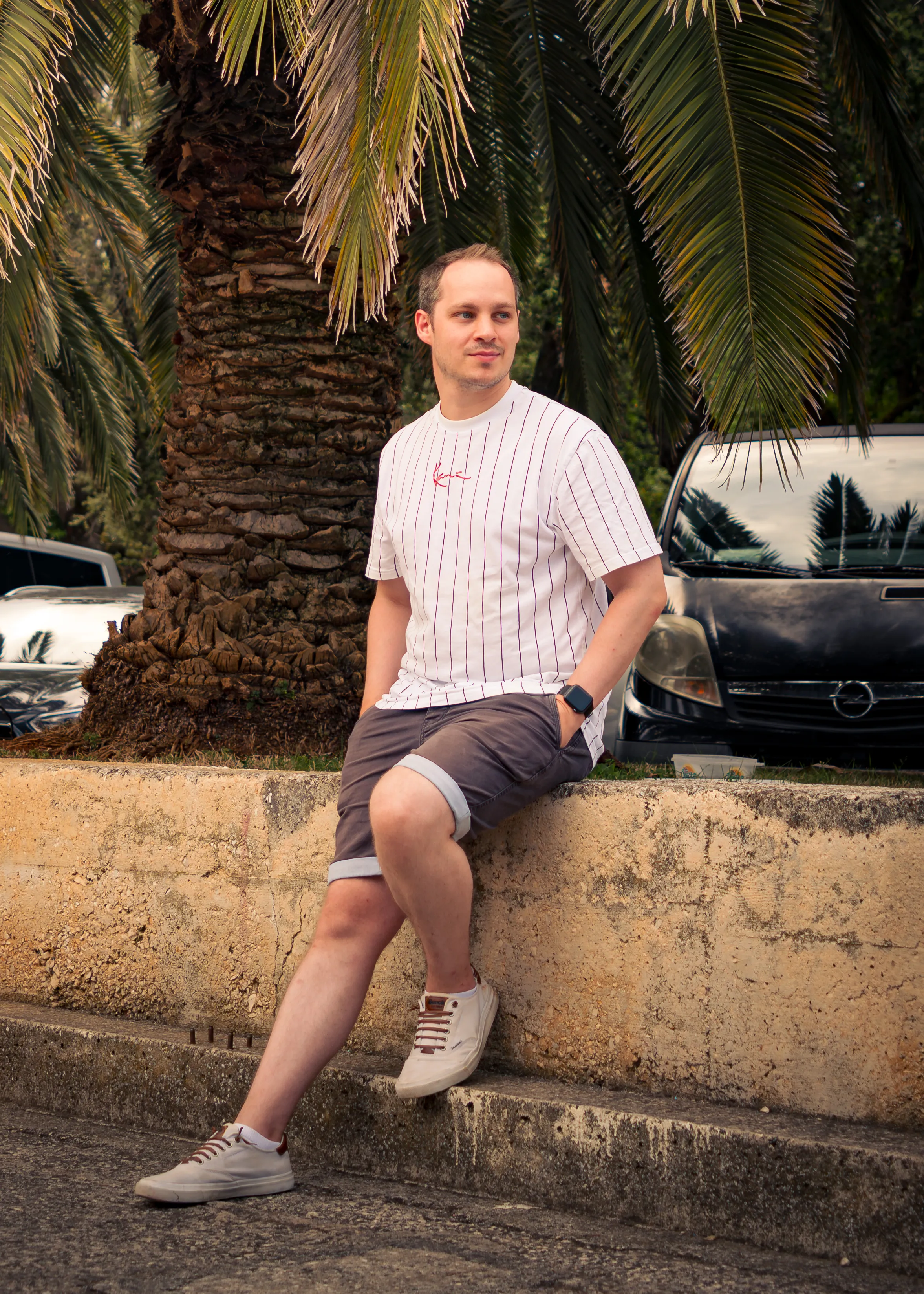 Sami Ekinci, Automotive-Filmmaker aus Wuppertal — an eine Mauer gelehnt, vor Palme und Fahrzeugen